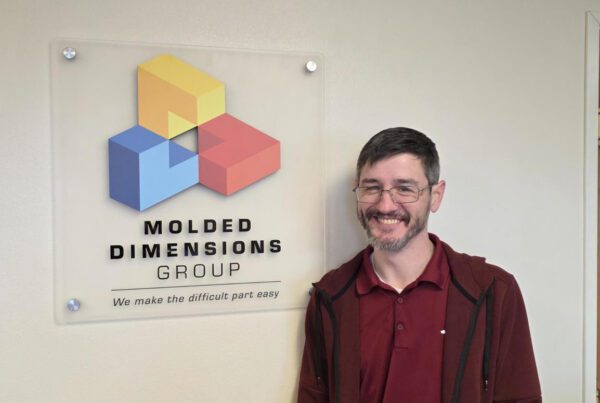 Ryan Piper standing next to the Molded Dimensions Group logo