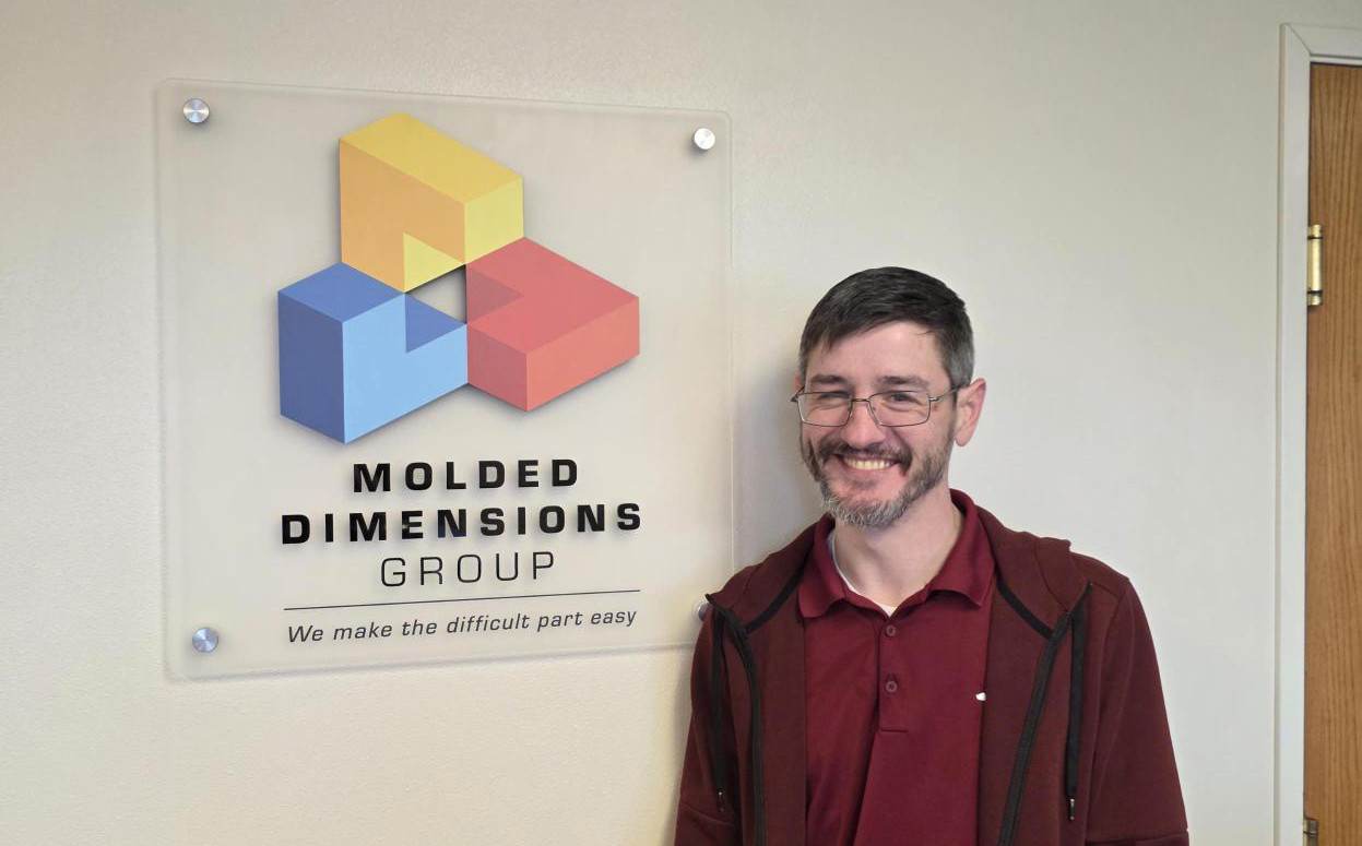 Ryan Piper standing next to the Molded Dimensions Group logo