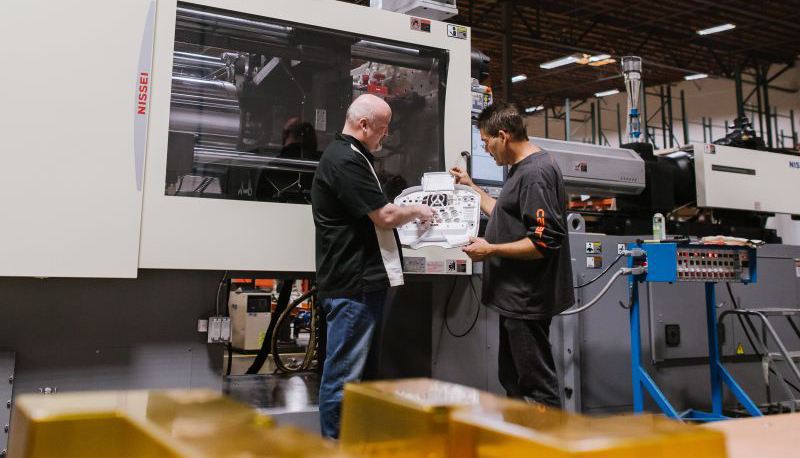 two men looking at plans for a rubber part discussing PFAS in front of a machine